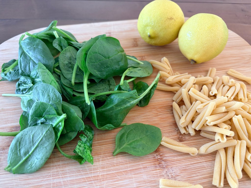 Spinach, lemons and pasta on a wooden chopping board